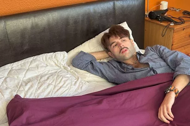 An image of a dark-haired man wearing pyjamas, lying in bed.