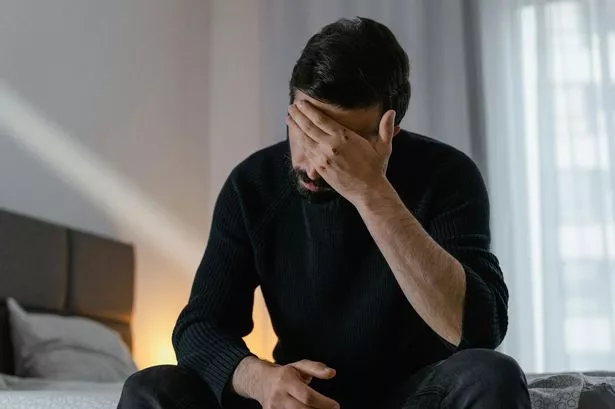 man sitting on edge of bed, stressed