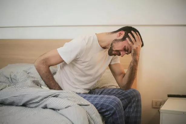 man sitting on edge of bed, stressed, unhappy