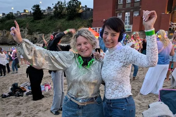 Sober Socials founder Viki Angel at a sober event with Heather Thompson - two women pictured dancing with earphones on on a beach, surrounded by happy crowds