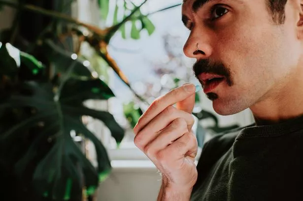 Simple image of a man putting a single blue pill into his mouth.