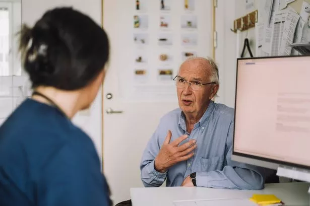 Senior male patient discussing with mature nurse during visit in clinic - stock photo