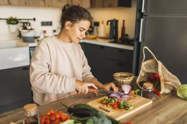 Young woman cutting fresh and raw vegetables on chopping board (stock photo)