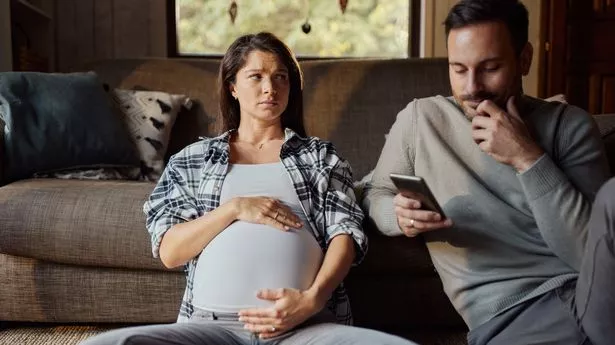 Depressed pregnant woman looking at her husband who is text messaging on cell phone at home.