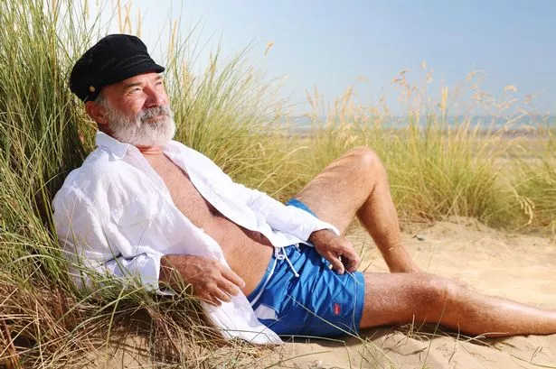 Captain Birds Eye lounges on beach in swim shorts as he models the summer swimwear range