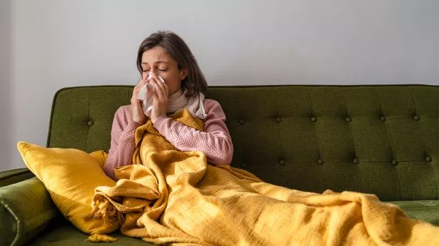 Sick woman blowing nose in facial tissue at home