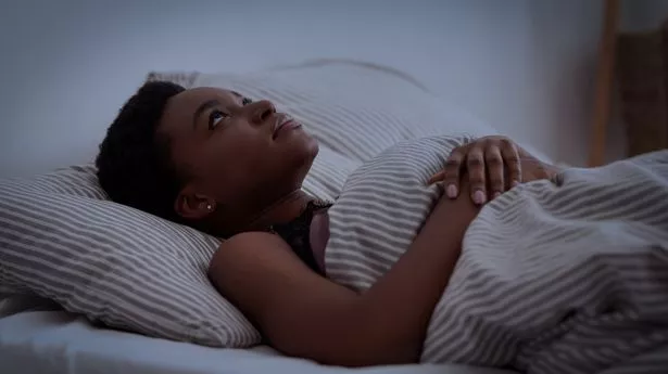 young woman lies on bed with blanket with open eyes