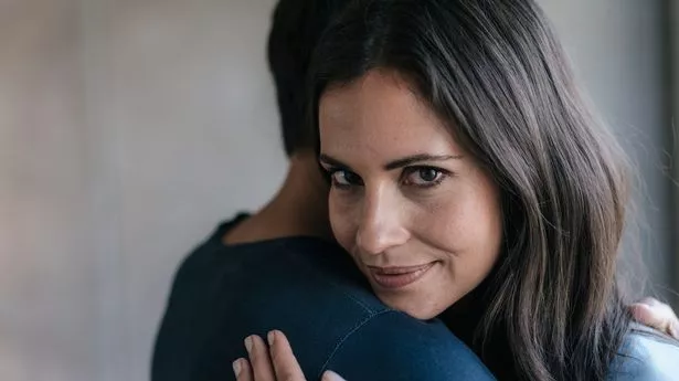 Woman hugging a man looking over his shoulder smiling