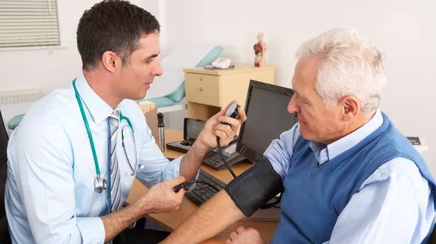 doctor taking senior man's blood pressure in surgery room having a check up