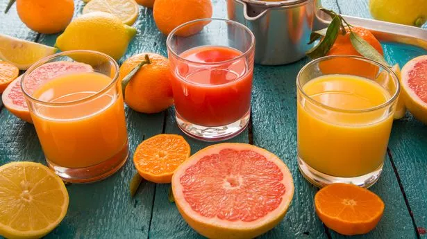 Multiple glasses of colourful red and orange fruit juices with orange slices on table