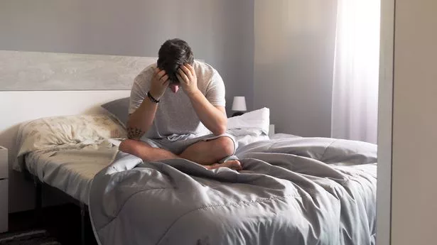 Man sits on the bed holding his head in his hands