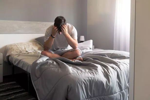 Man sits on the bed holding his head in his hands