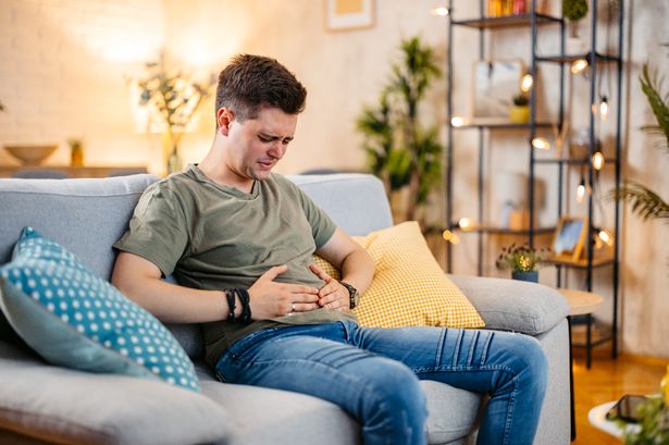 Young man having stomach pain while sitting on the sofa at home.