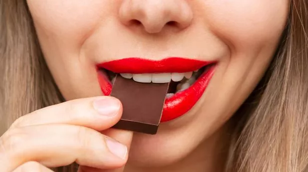 Cropped shot of a young caucasian blonde woman with glossy red color lips eating and enjoying delicious dark bitter chocolate. Close-up