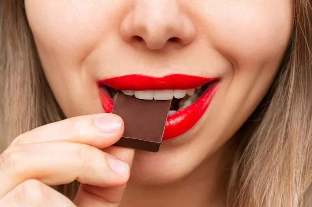 Cropped shot of a young caucasian blonde woman with glossy red color lips eating and enjoying delicious dark bitter chocolate. Close-up