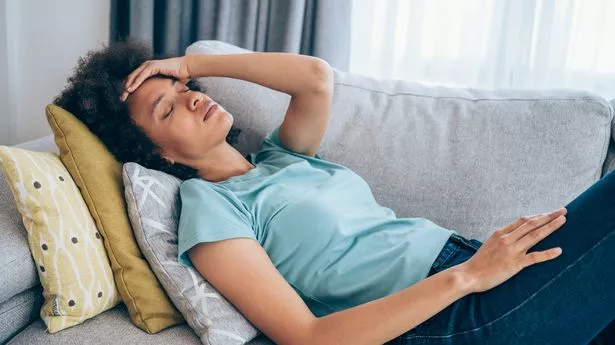 Sick young woman lying on the couch and holding her head with hand. Ill woman lying on the sofa with high temperature.