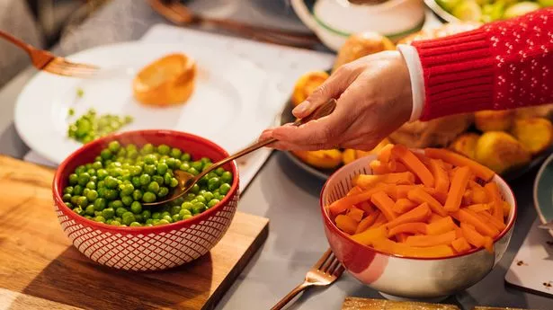 A woman is helping herself to some green peas as she gets a spoon full. Close -up.