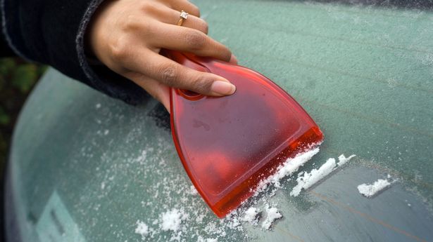 A young woman scraping ice from a frozen car windscreen with a red ice scraper