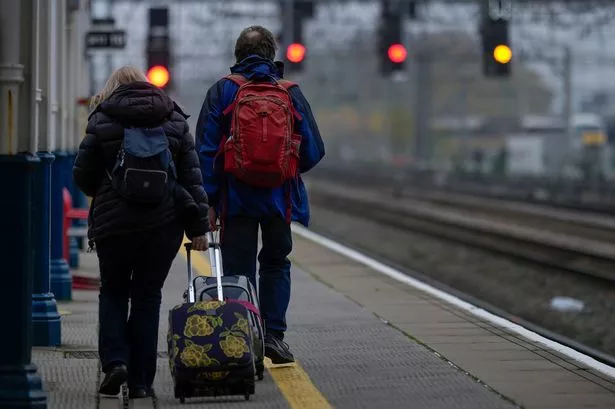 Back view of man and woman pulling suitcases down train platform