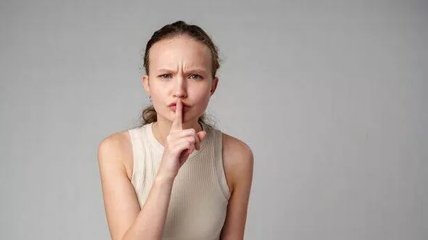 A photo of a woman holding her index finger to her lips - a gesture that signifies to be quiet