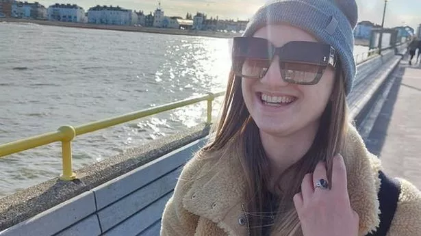 Millie Bull smiles for the camera at the seaside while holding a takeaway cup of coffee