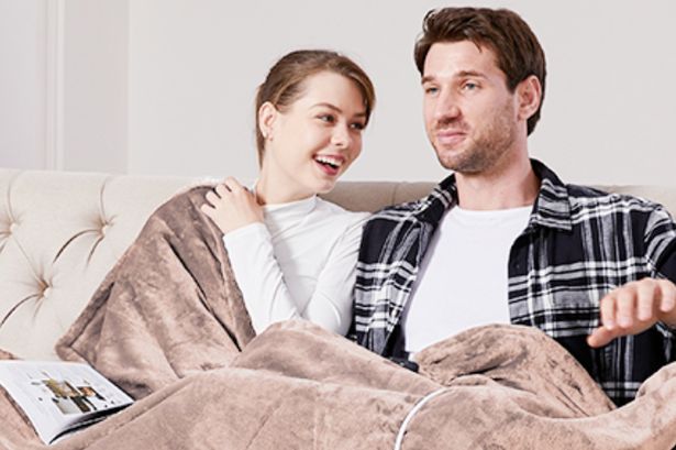 A woman and man sat under a brown blanket