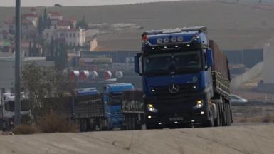 A convoy of blue lorries driving uphill on a slight bend 