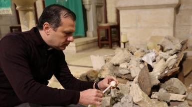 Reverend Munther Isaac lights a candle near a pile of rubble with baby Jesus figure lying on top inside the Evangelical Lutheran Church in Bethleham