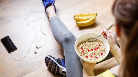 A woman sitting on the floor in exercise clothing a bowl of cereal