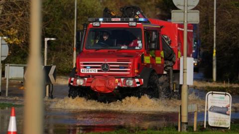 An emergency service vehicle drives through floodwater near the Billing Aquadrome in Northamptonshire