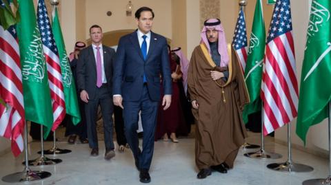  Marco Rubio walks with the Saudi Foreign Minister past US and Saudi Arabia flags