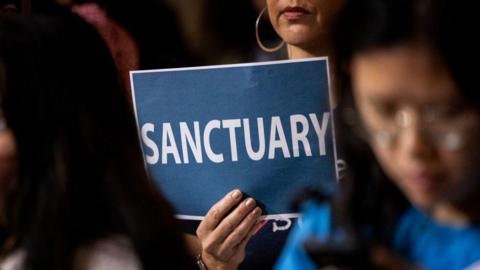 A woman in the audience holds up a poster with a message of support for immigrants as the Los Angeles City Council