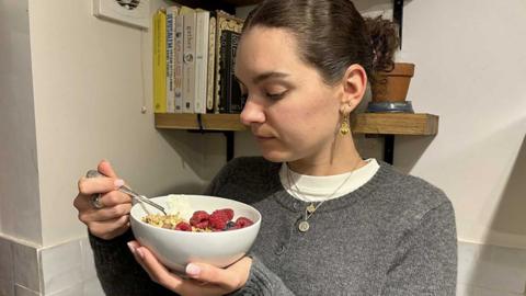 Woman eating a bowl of granola, raspberries and yoghurt