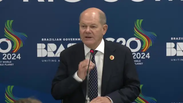 Headshot of Scholz sitting and speaking into a microphone