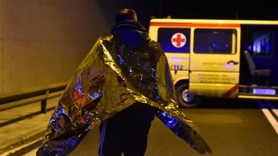 A man wearing a silver blanket stands near the ambulance