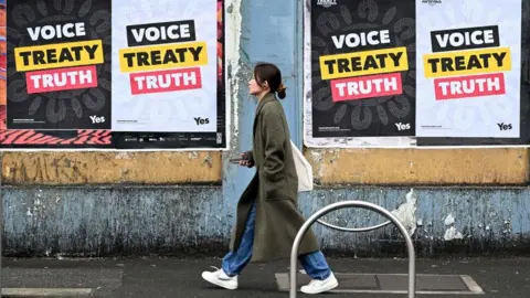 Getty Images A woman walks past posters advocating for an Aboriginal voice and treaty