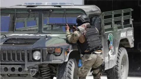 Reuters A member of the Haitian National Police takes cover behind a police vehicle while patrolling as ongoing gun battles between rival gangs have forced residents to flee their homes, in Port-Au-Prince, Haiti April 28, 2022