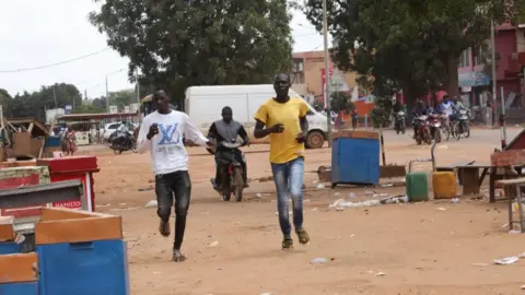 EPA Men run through a deserted marketplace in Burkina Faso's capital city Ouagadougou on Saturday