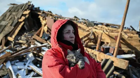 A lone woman holds a cat, surrounded by debris a day after a Russian strike, Ukraine: Resident Svitlana Vlasyk hugs her cat and looks at her house destroyed by yesterday's Russian missile strike, amid Russia's attack on Ukraine, in Chernihiv, Ukraine January 4, 2025