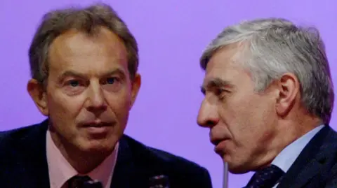 A close up of Tony Blair and Jack Straw's faces in conversation. They are wearing suits