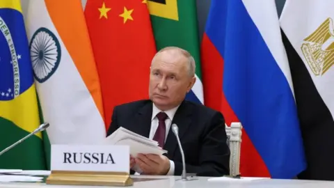 Getty Images Russian President Vladimir Putin takes part in a virtual Brics summit in November 2023 in front of the flags of member countries