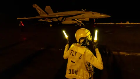 A flight deck crew member signals as an F/A-18 Super Hornet fighter jet takes off from the flight deck of the USS Dwight D. Eisenhower (CVN 69) aircraft carrier during operations in the southern Red Sea