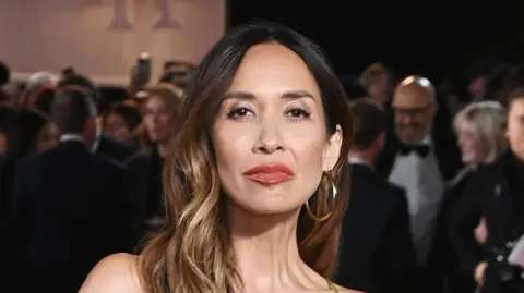 Myleene Klass looks straight on at the camera, she is wearing large gold hoop earrings and has her light brown wavy hair down