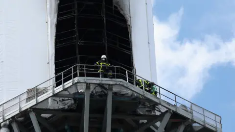 Reuters A close up photo of the plastic sheeting that was damaged by the fire. Two firefighters can be seen on the ledge surrounding the spire.