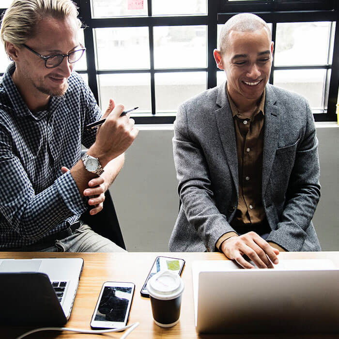 two people sitting next to each other look at one of their laptops