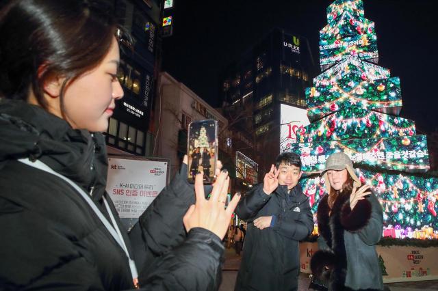 고객들이 서울 신촌 거리에 설치된 KT ‘팬메이드 K-AI아이디어 챌린지’ 팝업 미디어 트리 앞에서 기념 촬영을 하고 있는 모습