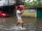 A man carries a cooking gas cylinder and wades past a waterlogged street in Chennai as the city witnesses torrential showers for the second time in five days.(AP)