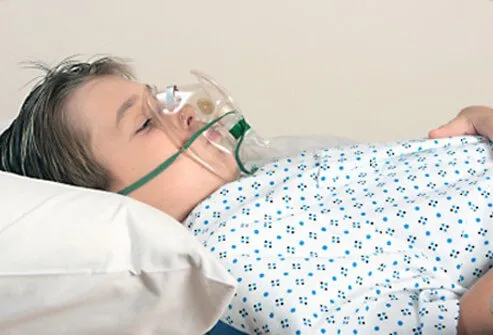 Boy laying in a hospital bed breathing with an oxygen mask.