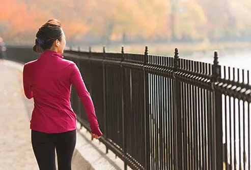 A woman walking outside along a park fence.