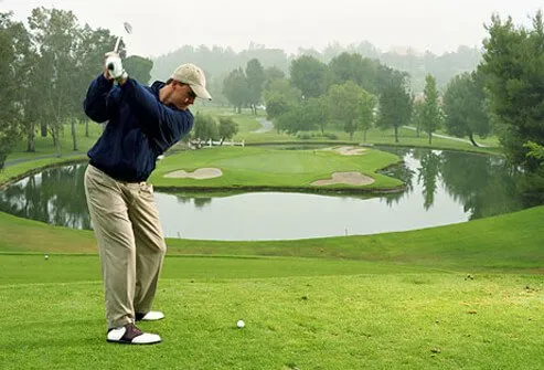 Golfer about to tee off on cool morning, protected from the sun.